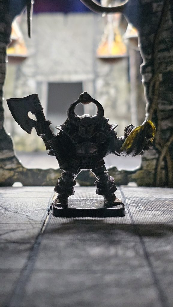Close-up of a painted original Hero Quest Chaos Warrior miniature. A classic black-armored warrior with axe and shield, standing on a textured base. One of Nathan’s early gaming miniatures.
