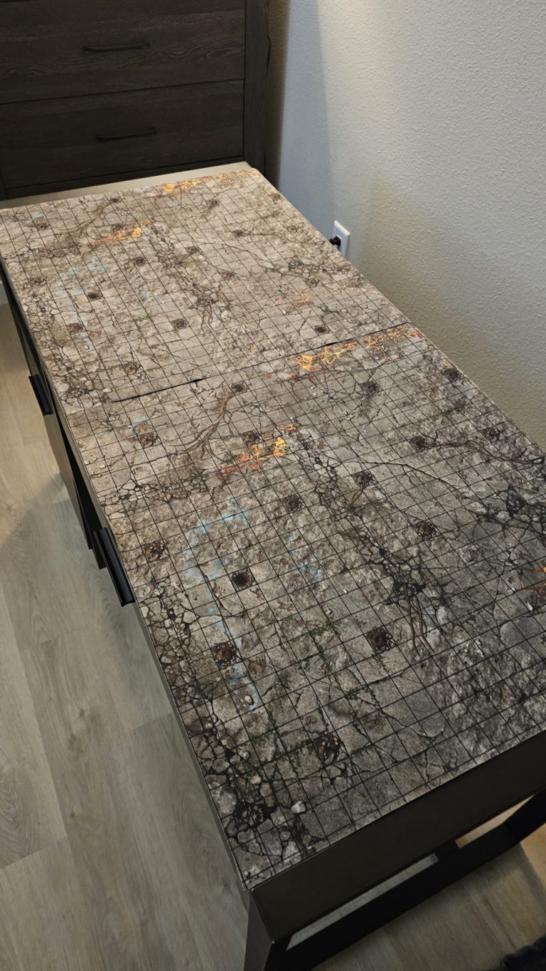 Clean 2x4 gaming table setup with a detailed camouflage battle mat in a modern apartment, marking the beginning of a new chapter after the house fire.
