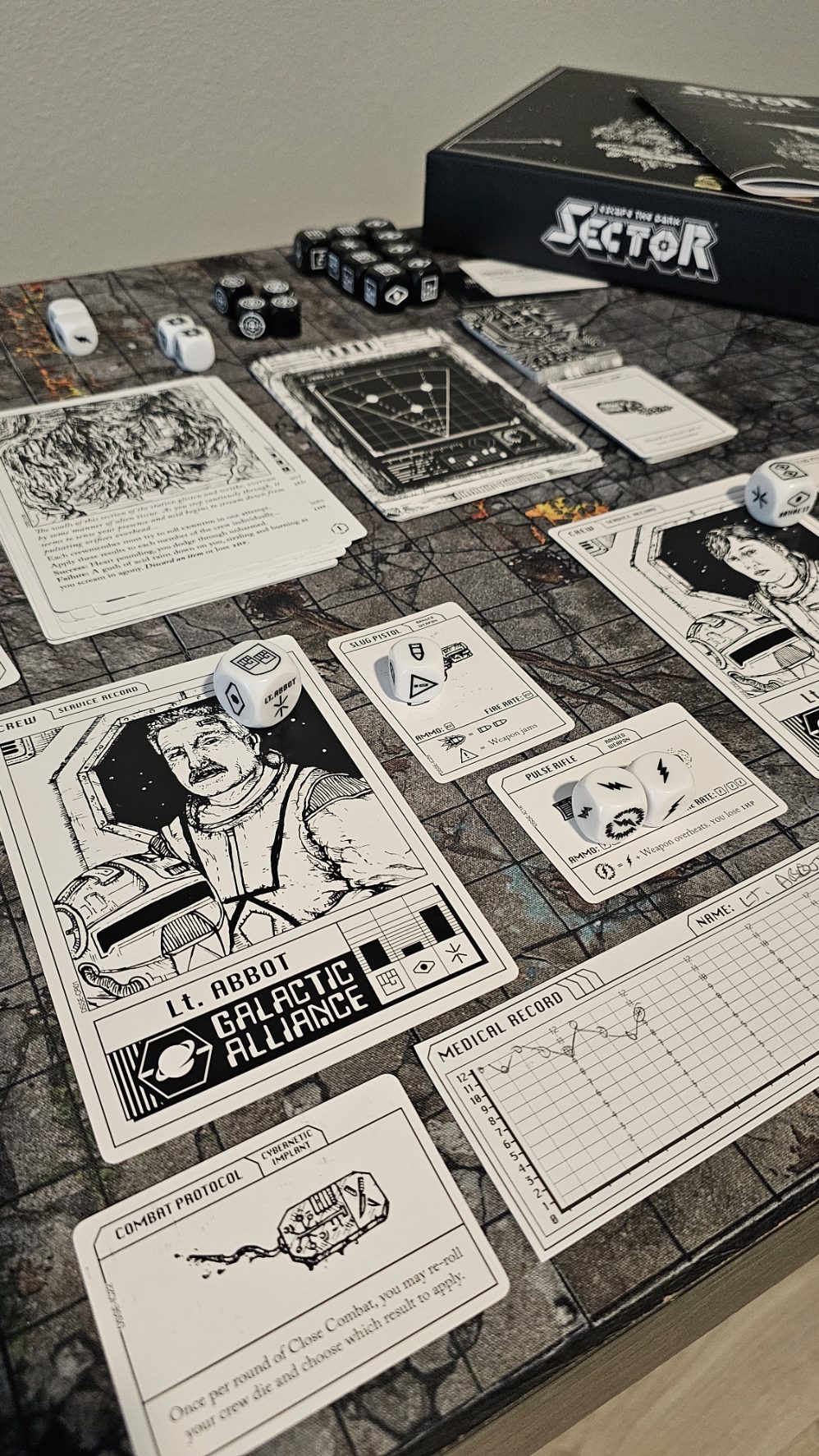 Escape the Dark Sector game setup on a textured gaming mat. Shows character cards including Lt. Abbott, dice, equipment cards, and the game box in the background. Dark sci-fi atmosphere with crew records and mission cards laid out for play.